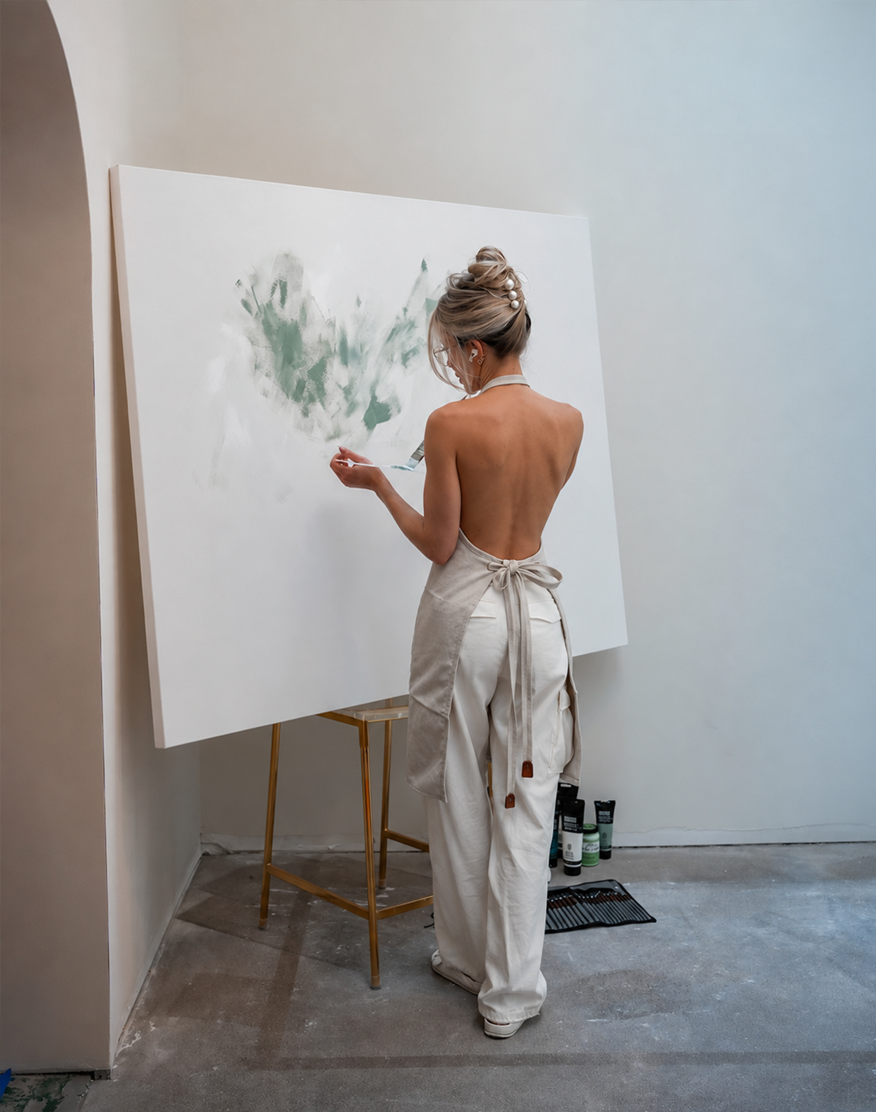 The artist in a linen apron painting a large canvas, seen from behind